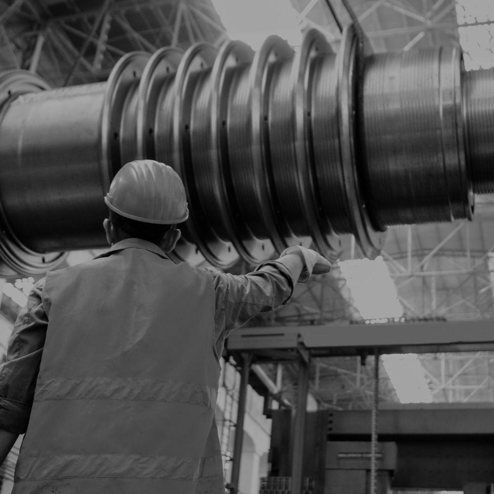 A person in a hard hat and reflective vest is overseeing the installation of a large industrial component, possibly in a factory or construction setting.